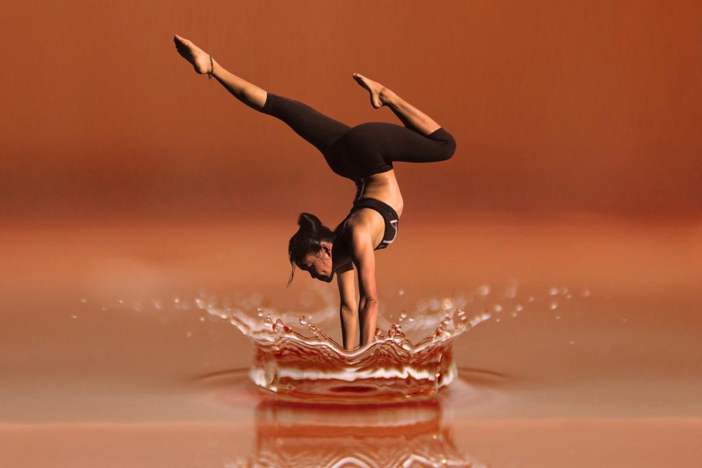 an actress working out by doing a handstand on the ground with water splashing around her hands and face
 