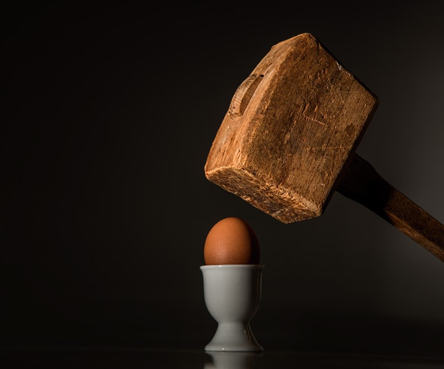 huge hammer about to smash an egg symbolizing fragility
